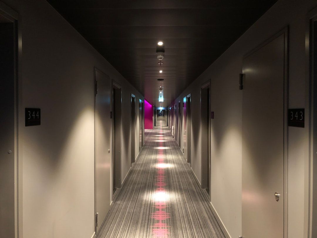 En lång hotellkorridor med grå dörrar och mönstrad matta.