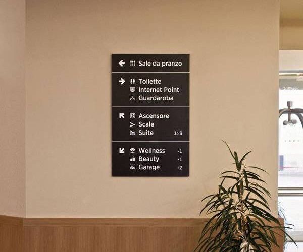 Svart hotellskylt med vit text som visar vägen till faciliteter.