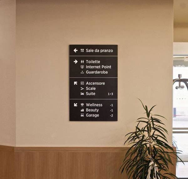 Svart hotellskylt med vit text som visar vägen till faciliteter.